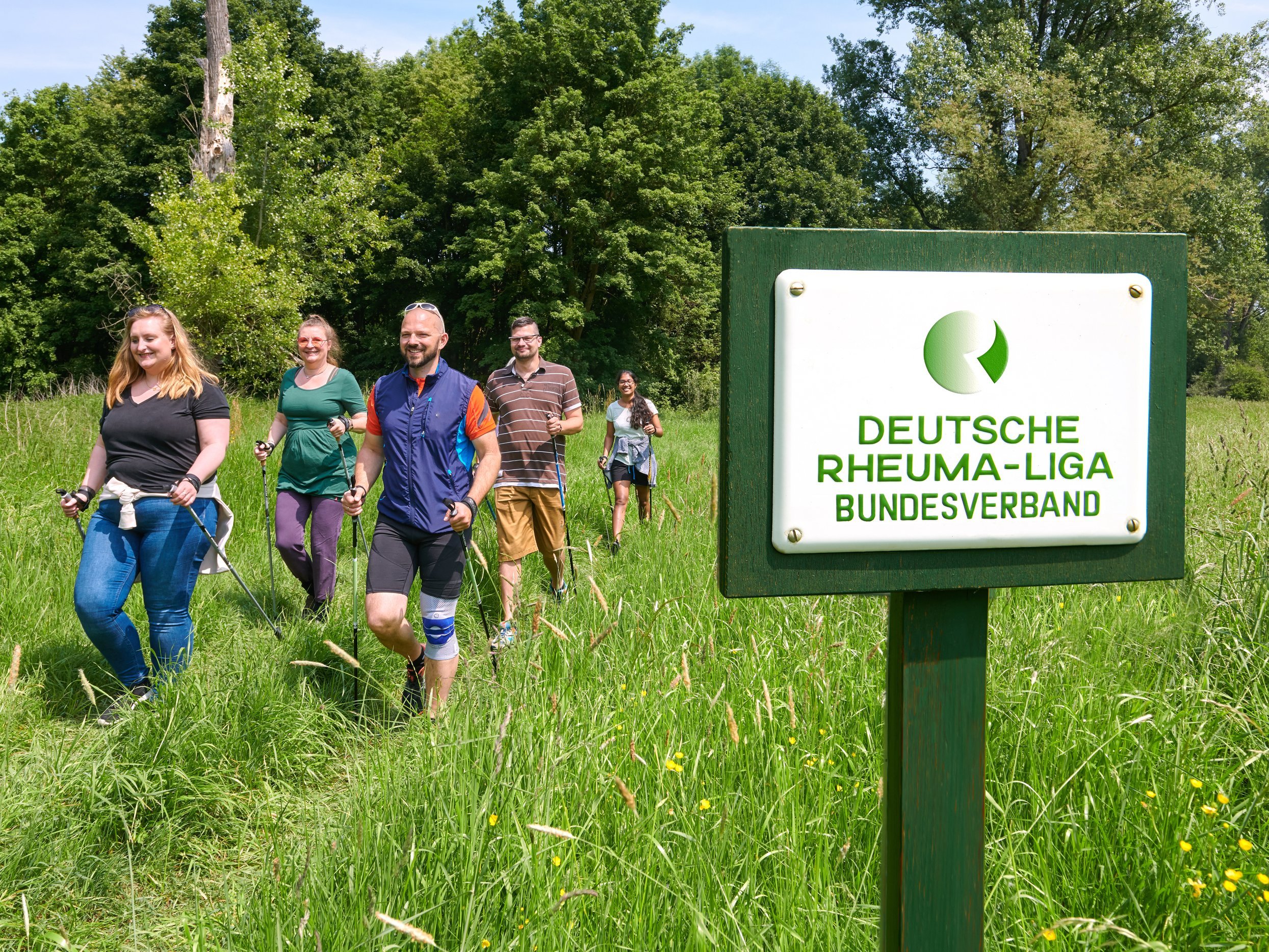 Gruppe von Menschen beim Nordic Walken, im Vordergrund Schild vom Deutschen Rheumaliga Bundesverband